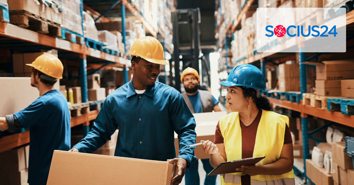 Group of warehouse workers in hard hats and safety gear, carrying boxes and clipboards