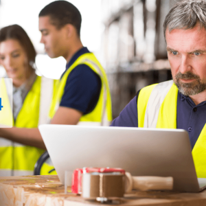 group in safety gear with a man using a laptop and phone in a warehouse