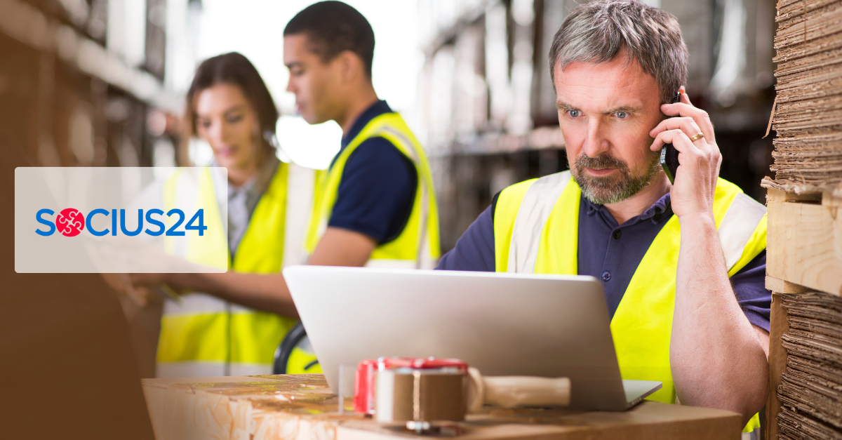 group in safety gear with a man using a laptop and phone in a warehouse